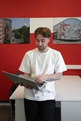 Poster - A focused IT specialist stands in a modern coworking area, engaging with his laptop while surrounded by colorful artwork that enhances the creative environment
