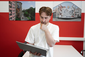 Poster - An IT specialist is focused on programming in a coworking environment, thoughtfully analyzing the information on his laptop in a creative workspace