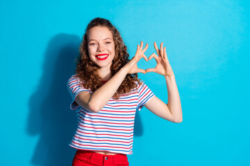 Poster - Cheerful woman making a heart shape with her hands against a bright blue background