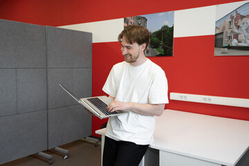 Poster - An IT specialist is focused on programming while standing beside a table in a vibrant coworking space. The room features colorful walls and personal artwork