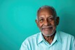 © kitipol - Elderly man in a dress shirt, smiling and looking directly at the camera, with a solid teal background and room for messaging