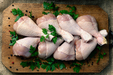 Raw chicken drumsticks arranged on a rustic wooden cutting board, accompanied by fresh parsley leaves and black pepper. This scene perfectly illustrates fresh ingredients ready for preparation