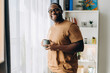 © Maria Vitkovska - Smiling African American man in glasses posing with cup of coffee in his apartment