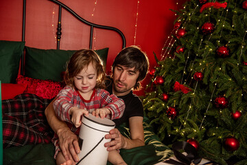 Young father and little daughter share joyful moment while unwrapping Christmas gift together in warmly lit, festive bedroom. Holiday spirit. Man and girl during the holiday break