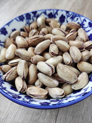 Fresh natural dried pistachios in a decorative plate on a wooden background