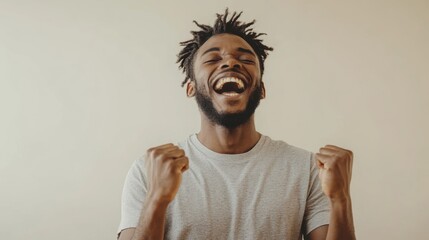 Happy man in a gray t-shirt, showing joy with raised fists against a neutral light background