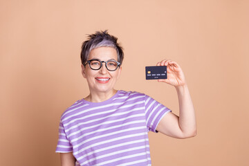 Poster - Photo of lovely nice woman wear striped stylish clothes hand hold bank card isolated on beige color background