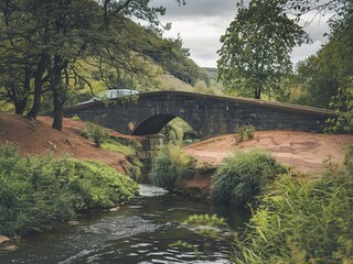 A stone bridge over a river with a car on the bridge, surrounded by trees and greenery