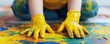 © Thanapipat - A child in yellow gloves creates colorful art with paint on a vibrant canvas, showcasing creativity and playful engagement.