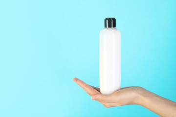 Wall Mural - Woman with shampoo bottle on light blue background, closeup. Space for text