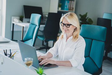 Wall Mural - Photo of it specialist in business development blonde hair woman sitting on workplace using laptop indoors loft modern office