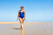 © Jacek Chabraszewski - Beautiful middle-aged woman in one-piece blue swimsuit and sunglasses walking on sandy beach in summertime. Front view. Armona Island, Portugal.