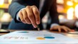 © Valentyna Prudnikova - Close-up of businessman's hand analyzing financial charts and graphs on desk, illustrating data-driven decision making in corporate strategy planning.