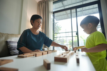 Wall Mural - Asian Grandmother playing wooden blocks game with young boy in living room, bonding and learning together.