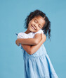 © Flashizzle/peopleimages.com - Self love, happy and child with hug in studio for sweet, embrace and development by blue background. Innocent, smile and little girl kid with gesture of care for affirmation, comfort and kindness