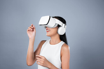 Smart female standing with gray background wearing VR headset connecting metaverse, futuristic cyberspace community technology. Elegant woman excited seeing generated virtual scenery. Hallucination.