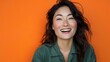 © jirayut - Radiating Happiness: A Woman's Infectious Smile Against a Vibrant Orange Backdrop.