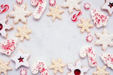 Poster - Christmas baking frame with an assortment of red and white theme cookies and candies. Top down view on a white marble background with copy space. Holiday candy cane baking concept.