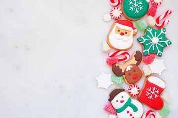 Poster - Cute colorful Christmas cookie side border on a white marble background with copy space. Top down view. Holiday baking concept.