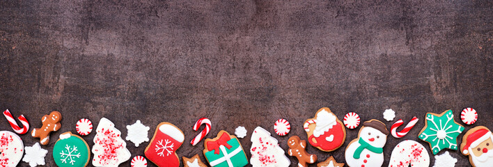 Poster - Fun colorful Christmas cookie bottom border on a dark stone banner background with copy space. Top view. Holiday baking concept.