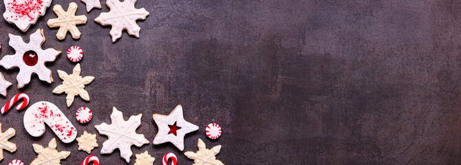 Wall Mural - Christmas baking corner border with assorted red and white theme cookies and candies. Top view on a dark stone banner background with copy space. Holiday candy cane baking concept.