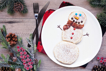 Wall Mural - Cute Christmas Snowman pancakes. Above view table scene against a wood background.