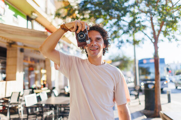 Photographer taking pictures on city street. Young tourist smiling happily using camera during city walk.