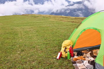 Tent, backpack and camping equipment on green grass in mountains, space for text