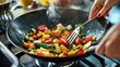 © Business Pics - close up of hands cooking vegetables in a wok on a stove at home, using fork and spoon, colorful vegetable mix, healthy breakfast, high quality photo, blurred background