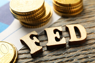 Letters Fed (Federal Reserve System) and coins on wooden table, closeup