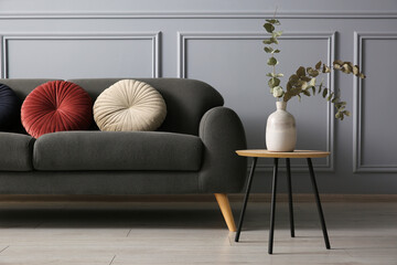 Canvas Print - Stylish sofa with cushions and eucalyptus branches in vase on coffee table near grey wall