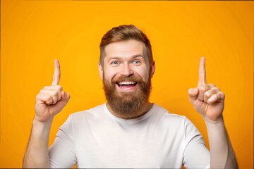 Portrait of a happy bearded man pointing fingers up at copyspace isolated over yellow background
