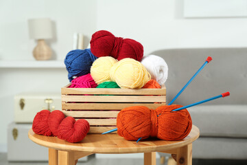 Canvas Print - Skeins of soft yarn in crate and knitting needles on wooden table indoors