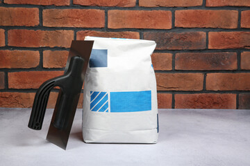 Poster - Bag of cement and plastering trowel on light textured table against red brick wall