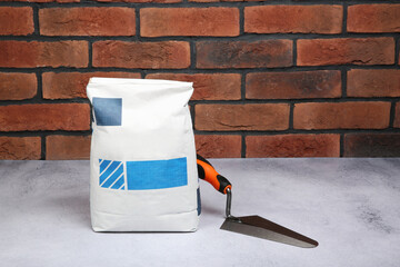 Canvas Print - Bag of cement and trowel on light textured table against red brick wall. Space for text