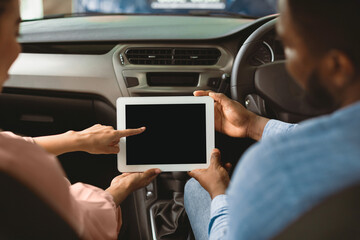 Afro Couple Using Digital Tablet With Empty Screen Sitting In New Car In Dealership Center. Mockup, Back View, Selective Focus