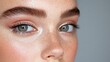© Elysian Essence - Close-up of freckled face with blue-green eyes, shimmering eyeshadow, long lashes and natural brows, glowing skin with a radiant finish, studio portrait highlighting beauty and detail