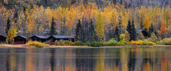 Wall Mural - panoramic view of autumn trees and vacation cabins with reflections in the lake in alaska.