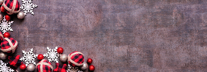 Wall Mural - Christmas corner border of red and black gingham ornaments, baubles and snowflakes. Overhead view on a dark brown banner background. Copy space.