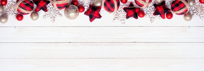 Wall Mural - Christmas top border of red and black plaid check ornaments, snowflakes and baubles. Overhead view on a white wood banner background. Copy space.