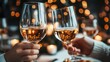 © familymedia - In a dimly lit setting, two hands softly clink wine glasses together, capturing the essence of warmth, intimacy, and celebration during a special evening occasion.