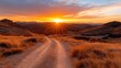 © familymedia - A sunlit road winds through rugged, mountainous terrain as the golden hour paints the sky with vibrant hues, creating a sense of adventure and exploration at dusk.