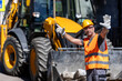© zphoto83 - Construction worker directing traffic near heavy machinery at a busy job site during daylight hours