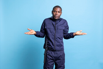 Confused african american guard shrugging in the studio, raising his shoulders to do an i dont know gesture. Security agent being clueless and uncertain on camera, unsure about something.