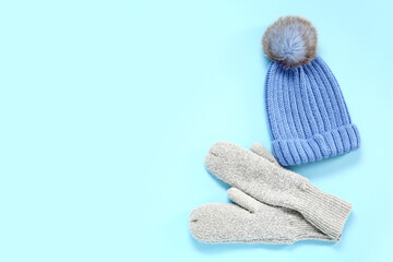 Warm mittens and hat on color background