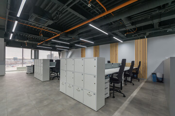 The interior of a modern office with panoramic windows. An open space with cabinets, tables and ergonomic chairs.