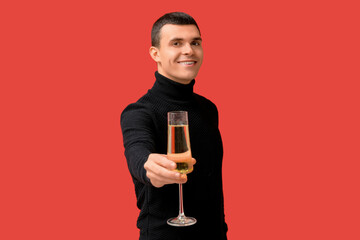 Poster - Happy young man with glass of champagne celebrating Christmas on red background