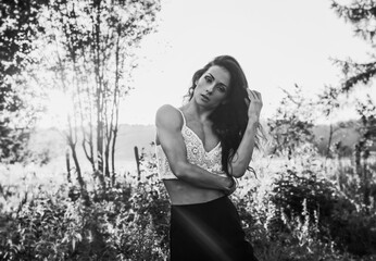 Beautiful sexy female model looking front with long brown hair style on sunset red orange summer background among the trees. Black and white portrait