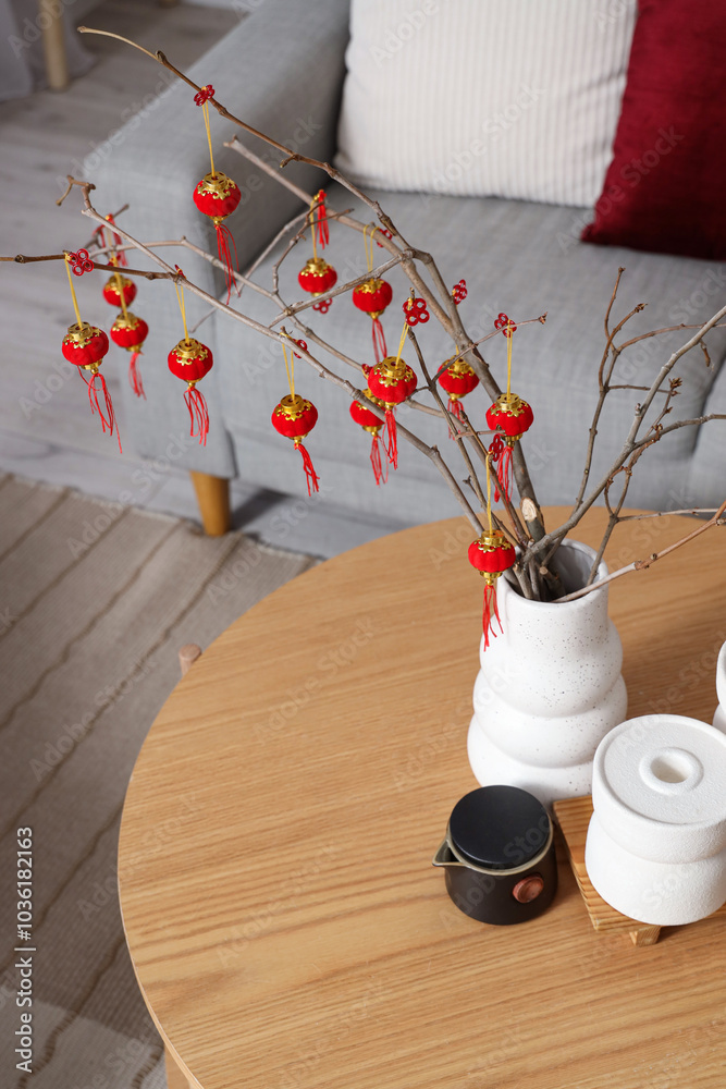 Vase with tree branches, Chinese lanterns and teapot on table in living room. Chinese New Year celebration