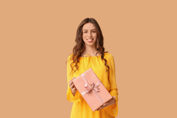 Wall Mural - Happy young woman with gift box on beige background